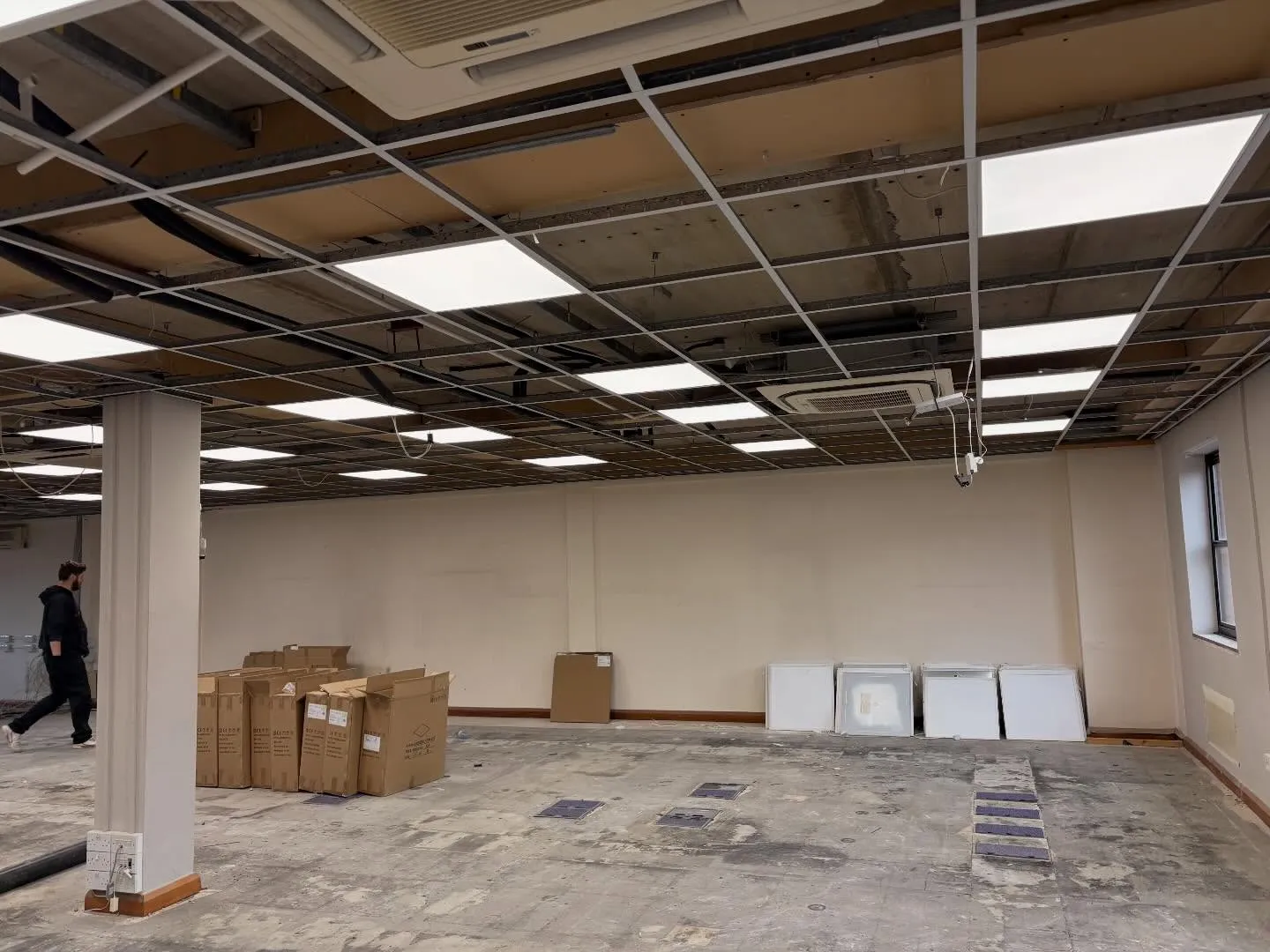 New LED panel lighting being installed into a suspended ceiling grid on an office floor in Weybridge