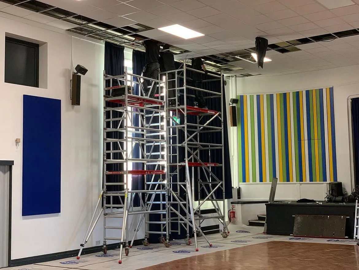 Engineers on mobile access towers installing galvanised cable tray in a school hall in Surrey
